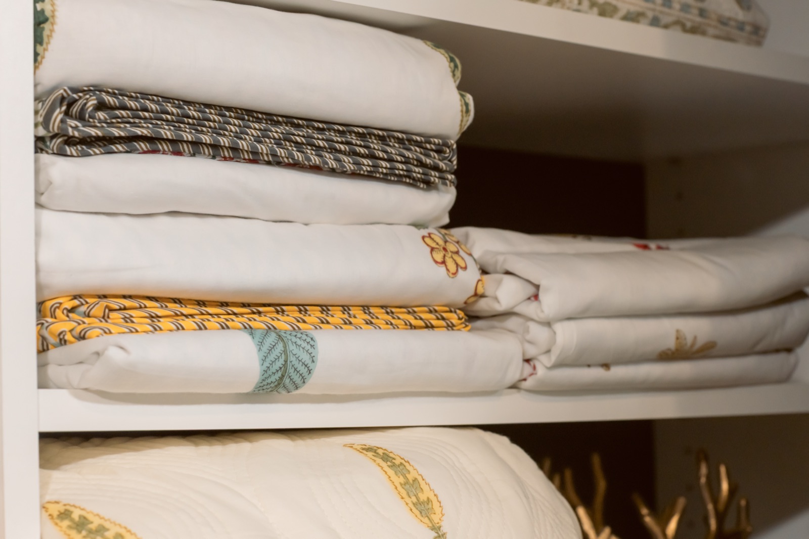 Folded block-print bedding stacked on a linen shelf